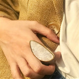Fashion woman ring with large white stone worn on hand with brown coat and white shirt background