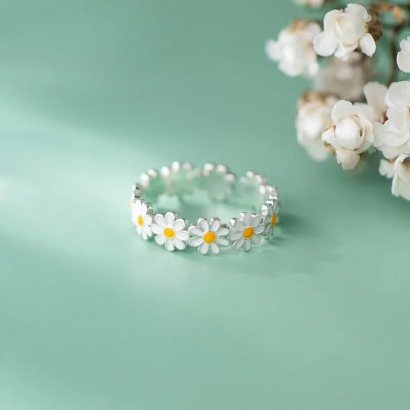 Silver ring with white and yellow daisy flowers on green background and white flowers blurred in the corner pink romantic flower rings